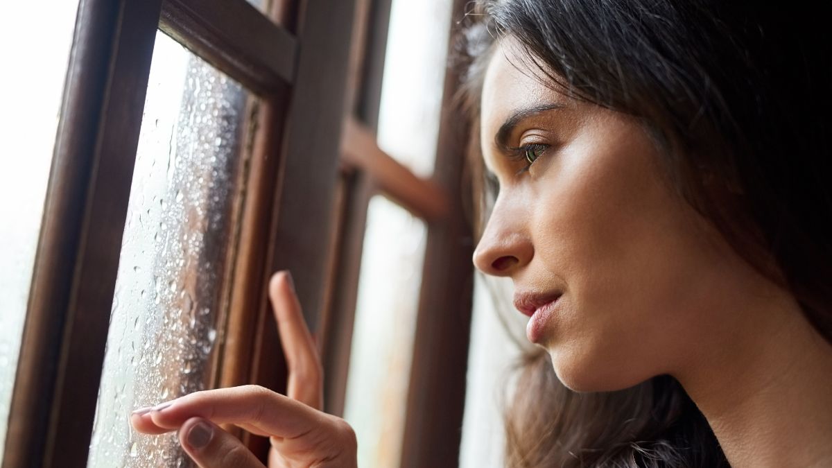 A woman looking out a window on a dark, rainy day, reflecting the mood and reduced daylight associated with Seasonal Affective Disorder.