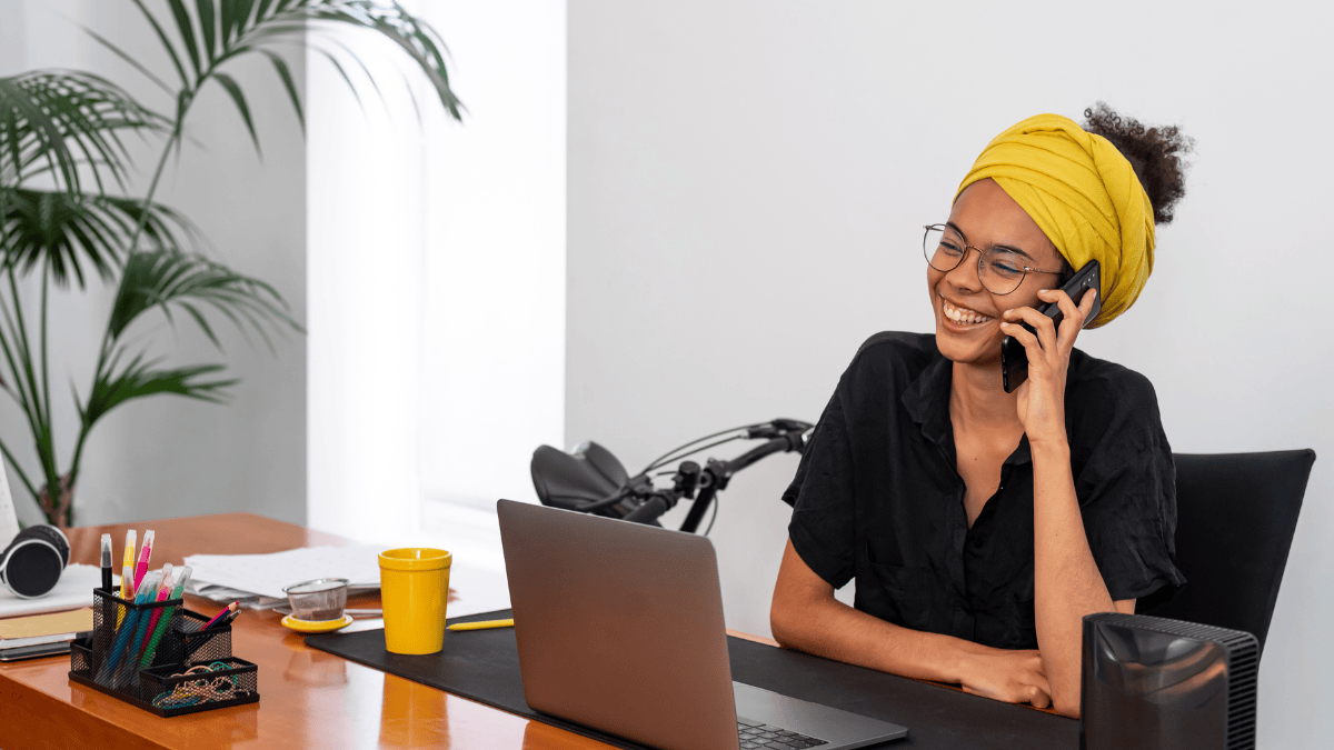 A professional woman smiling while speaking on the phone at her desk, demonstrating engaged and active listening during a work conversation.
