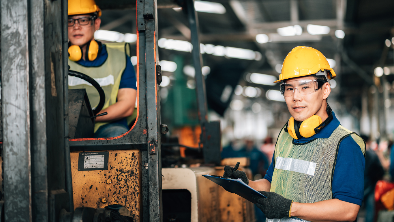 Factory workers wearing helmets and safety gear operating machinery and completing a safety checklist in a manufacturing facility