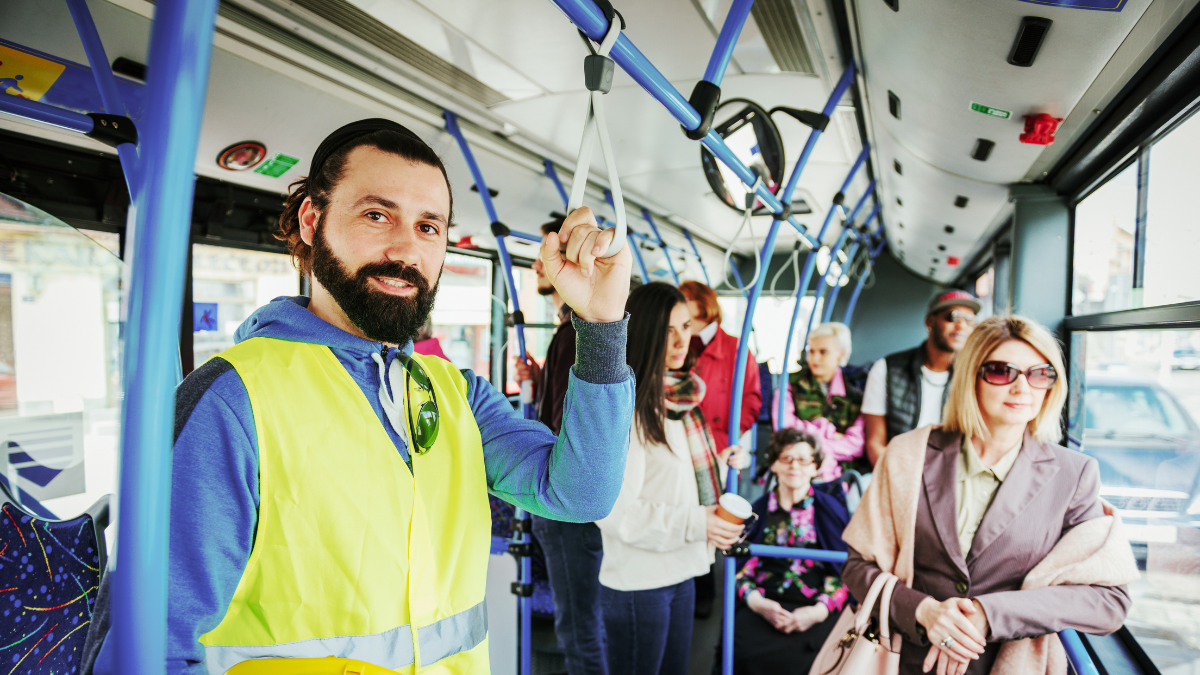 Transit worker standing on a bus with passengers during a daily commute.